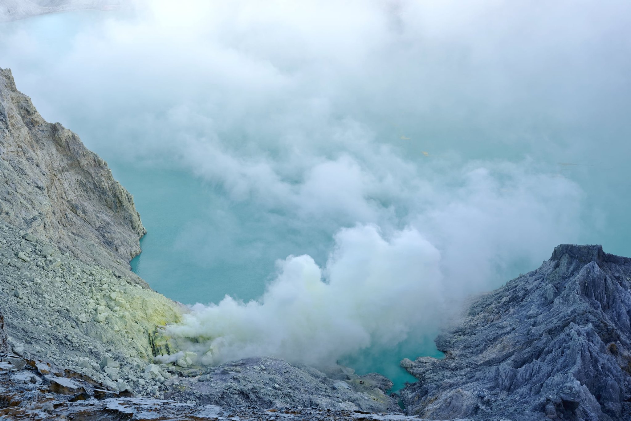 The turquoise acid lake in the crater of Kawah Ijen, East Java, with sulphur smoke rising from the vents on its shore